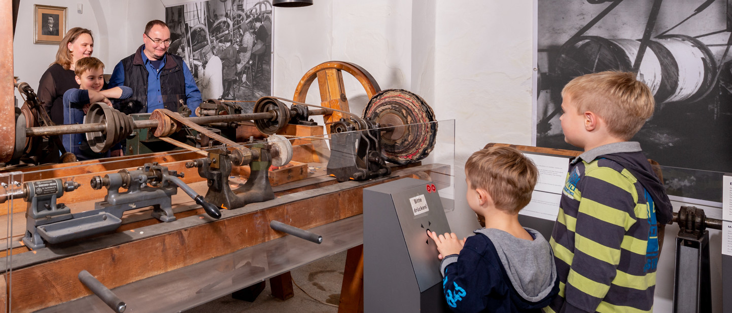 Familie betrachtet eine historische Maschine aus der Knopfindustrie